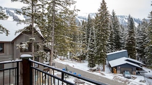 A cabin with a garage, a covered driveway, and a snow-covered landscape with trees and mountains in the background.