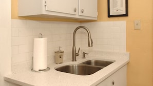 Una cocina con un lavamanos doble, encimera con motas blancas y un dispensador de toallas de papel.