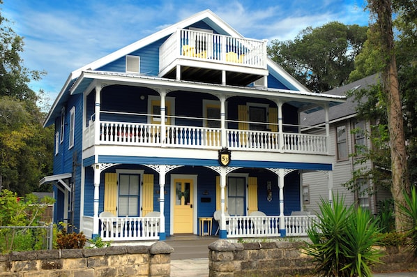 Une maison à deux étages dotée d’un balcon, d’un porche à l’avant et d’un mur en pierre à l’extérieur.