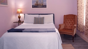 Un dormitorio con cama, una silla, una lámpara y un cuadro en la pared.