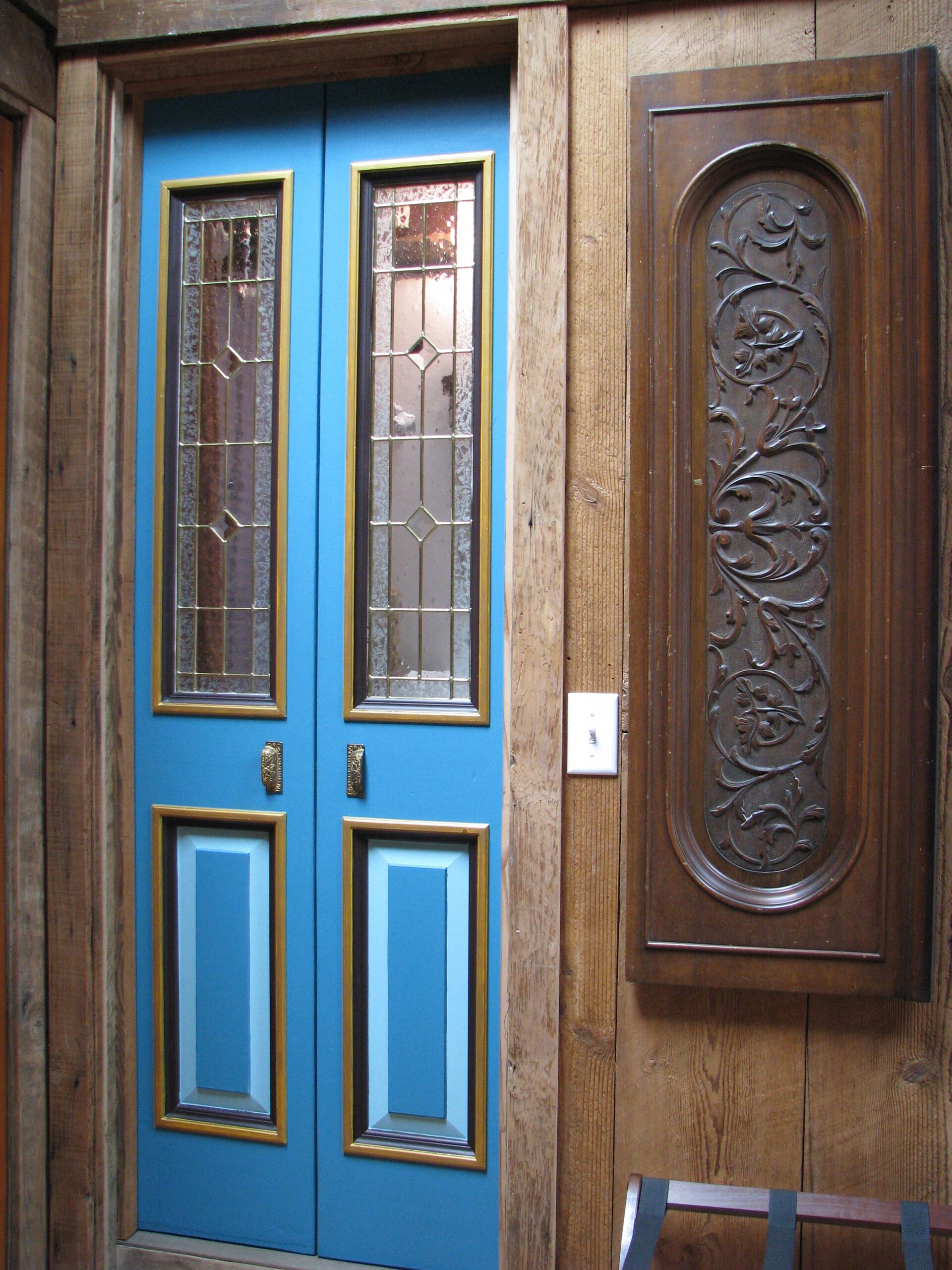 Una puerta azul con dos paneles de vidrio y un panel de madera con un diseño ornamentado.