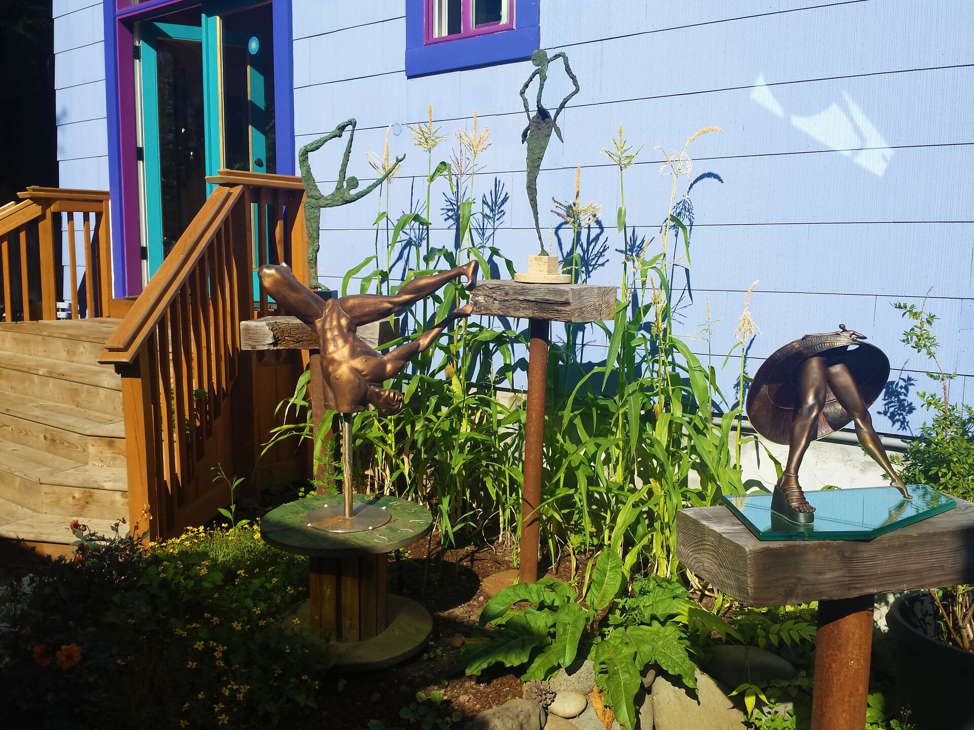A garden with sculptures, a wooden deck, and a building with a blue exterior.