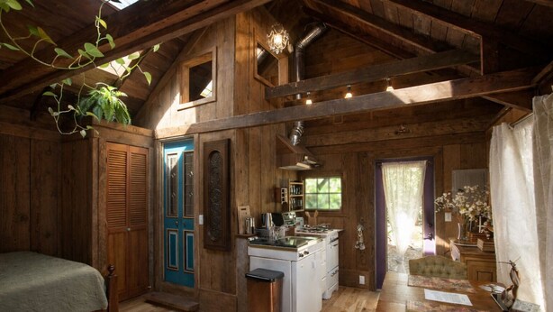 Interior rústico de uma cabana, com cama, cozinha compacta e área de refeições.