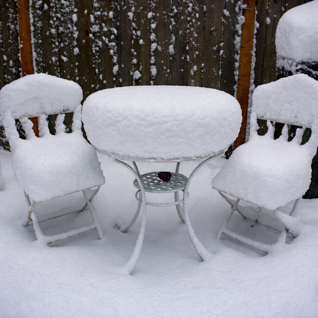 A snow-covered outdoor seating area with a metal table and two chairs.