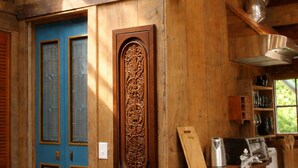 Interior rústico de cabana de madeira com porta azul, um entalhe de madeira na parede e uma área de cozinha com cafeteira e utensílios.