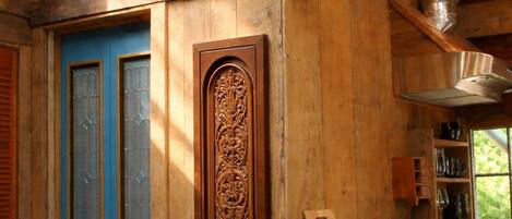 A rustic wooden cabin interior with a blue door, a wooden carving on the wall, and a kitchen area with a coffee machine and utensils.