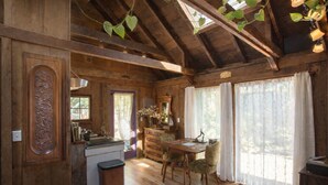 Interior rústico de cabana com paredes e teto de madeira, área de jantar com mesa e cadeiras, e cozinha com pia e armários.