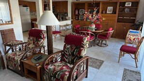 Sala de estar con muebles de mimbre, ventilador de techo y comedor con mesa y sillas.