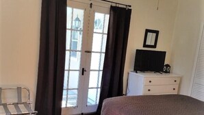 Une chambre à coucher comprenant un lit, une table de chevet, une chaise, un ventilateur de plafond et une fenêtre avec des rideaux.