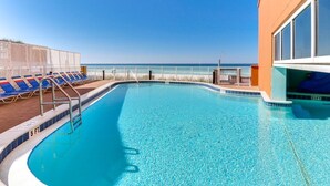 Ein Pool mit klarem, blauem Wasser, umgeben von Liegestühlen und einem Geländer, mit Blick auf den Ozean.