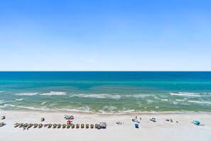 A beach with rows of umbrellas and beach chairs, a clear blue sky, and calm ocean waves. - Tropic Winds CORNER West Unit -Deluxe Ocean Front-FREE Beach Service March-Oct. (Panama City Beach)