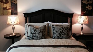 Ein ordentlich bezogenes Bett mit dunklem Kopfteil, flankiert von zwei Nachttischen mit Lampen, und zwei an der Wand befestigten floralen Bildern.