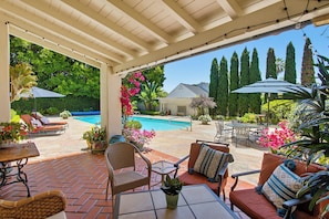 Un patio cubierto con mobiliario exterior, una piscina y un jardín.