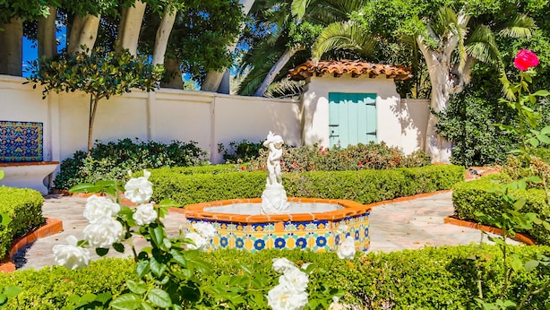 Ein Garten mit einem Brunnen, geschnittenen Hecken und einem Gebäude mit einer blauen Tür.