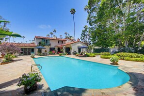 Una piscina rodeada de un patio y una casa al fondo.