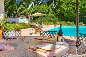 Mesa de comedor dispuesta con copas de vino, platos y cubiertos, con vistas a una piscina y abundante vegetación.