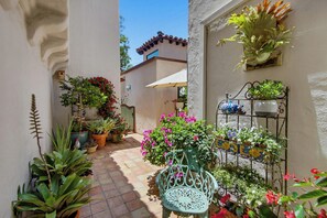 A narrow courtyard with potted plants, a metal chair, and a tiled floor. - Romantic Spanish Home, Private Pool, Walk to Beach (La Jolla)