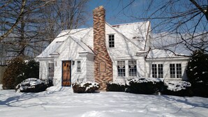 Une maison recouverte de neige, avec une cheminée en briques, une façade blanche et de nombreuses fenêtres.