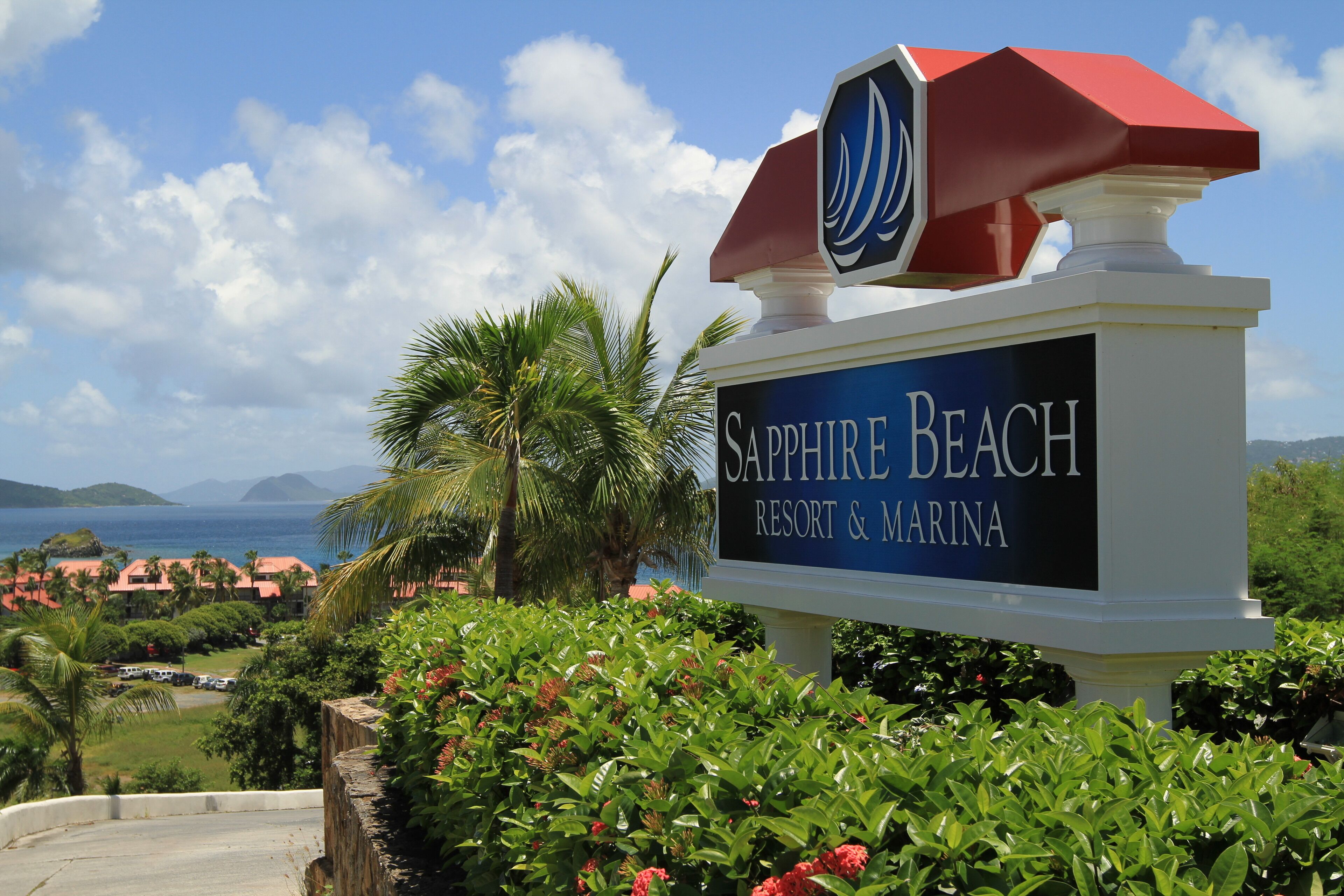 Naamplaatje voor Sapphire Beach Resort & Marina, met uitzicht op de oceaan en palmbomen op de achtergrond.