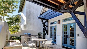 Eine Terrasse mit Grill, Esstisch und Stühlen, umgeben von einer Betonmauer und einer blauen Tür.