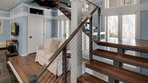 Ein geräumiger Wohnbereich mit einer Holztreppe, einem weißen Sofa und einer Decke mit freiliegenden Balken.