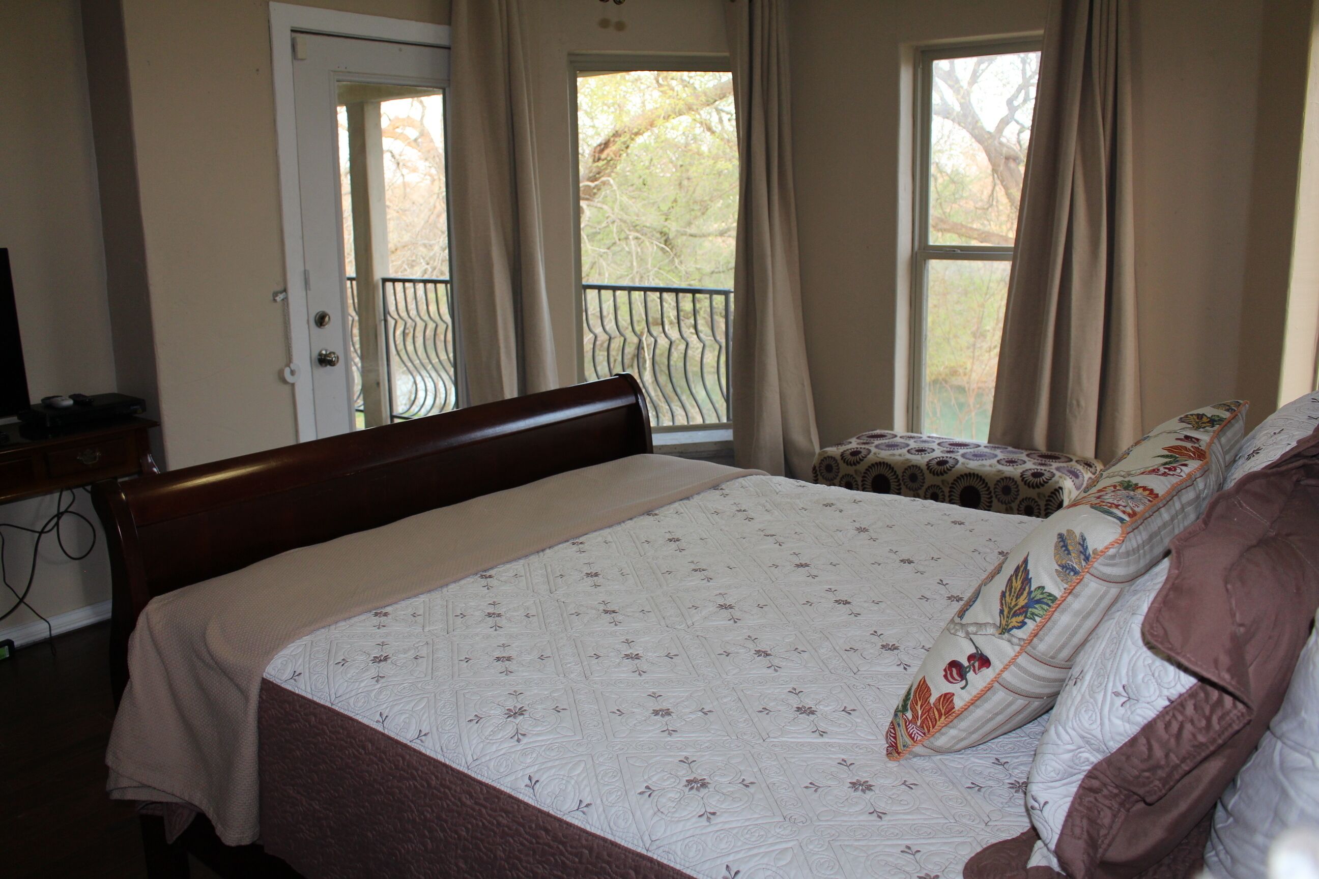 Une chambre à coucher avec un grand lit, une table de chevet, une chaise et une fenêtre avec des rideaux.