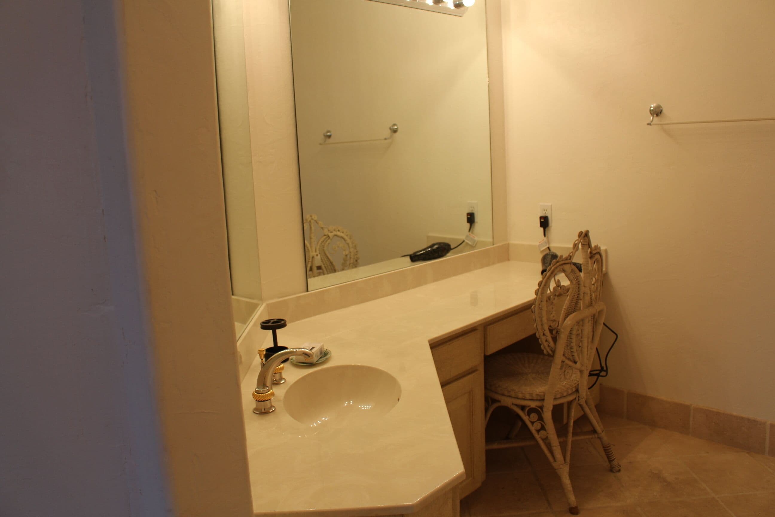 A bathroom with a large mirror, a sink, and a chair.