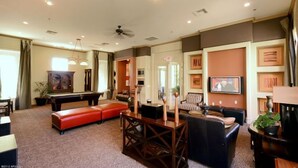 A spacious living room with a pool table, comfortable seating, a ceiling fan, and a television.