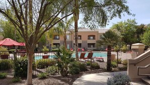 A pool area with lounge chairs and umbrellas, surrounded by a fence and greenery.