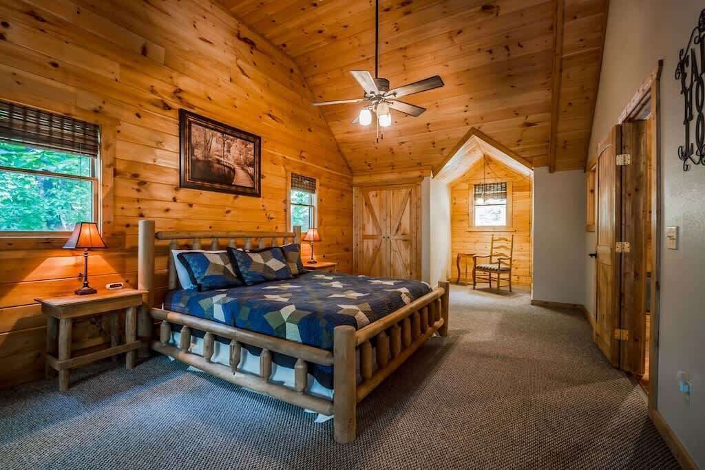 Une chambre située dans une cabane en rondins, avec un lit, un ventilateur de plafond et un petit coin salon.