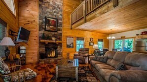A log cabin interior with a fireplace, wooden walls, a sofa, and a television.