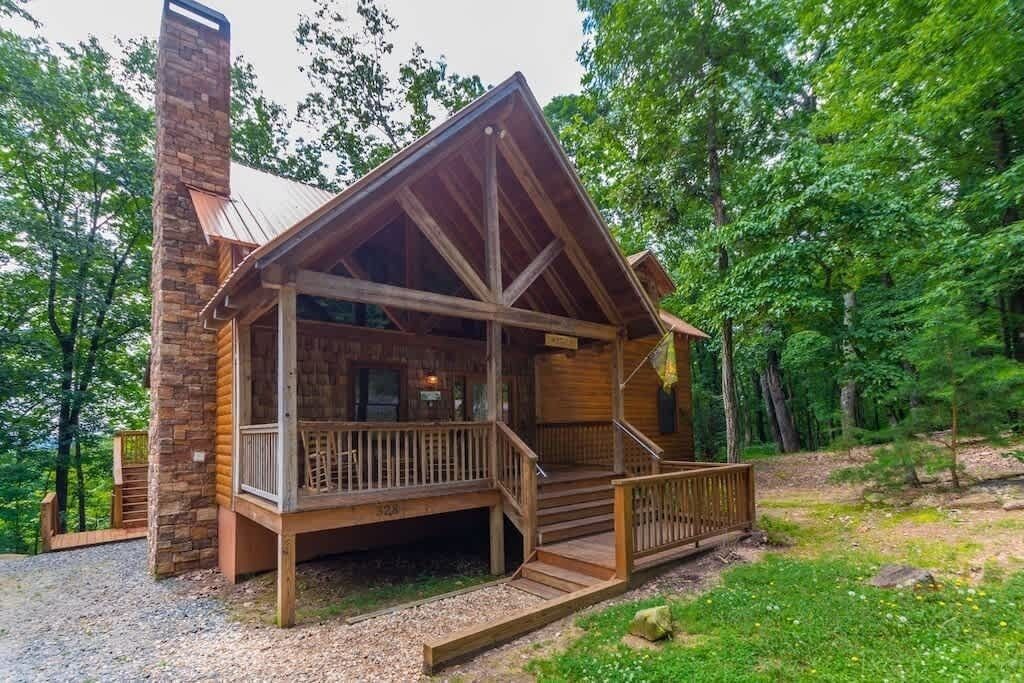 A log cabin with a porch, a chimney, and a gravel driveway.