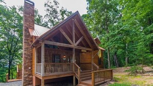 A log cabin with a porch, a chimney, and a gravel driveway.
