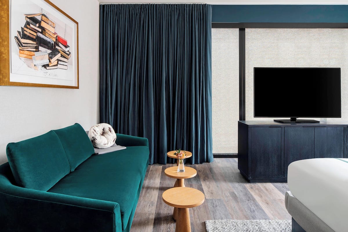 Une chambre d’hôtel moderne avec un canapé de couleur turquoise, une petite table en bois, un téléviseur à écran plat et un lit.