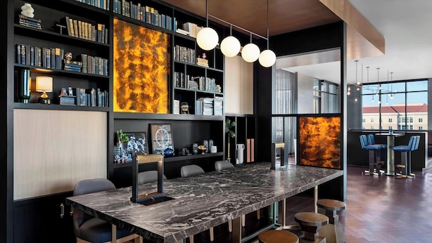 A modern bar area with a marble countertop, bar stools, and a bookshelf filled with books and decorative items.