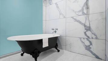 A bathroom with a freestanding bathtub, white marble tiles, and a hexagonal floor pattern.