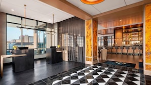 A modern hotel lobby with a reception desk, a bar area, and a patterned floor.