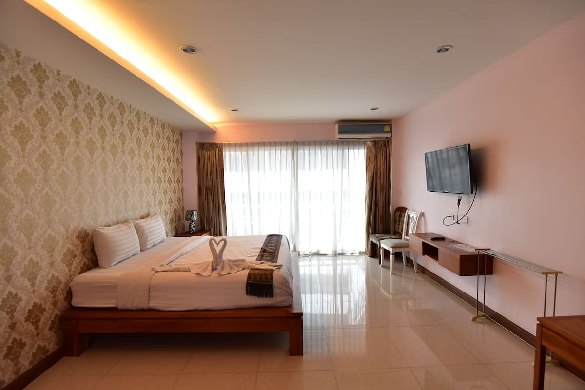 A hotel room with a bed, a desk, a chair, a television, and an air conditioning unit.
