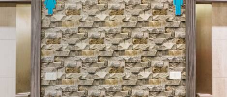 Pared con diseño de piedra y dos símbolos de género sobre una puerta.