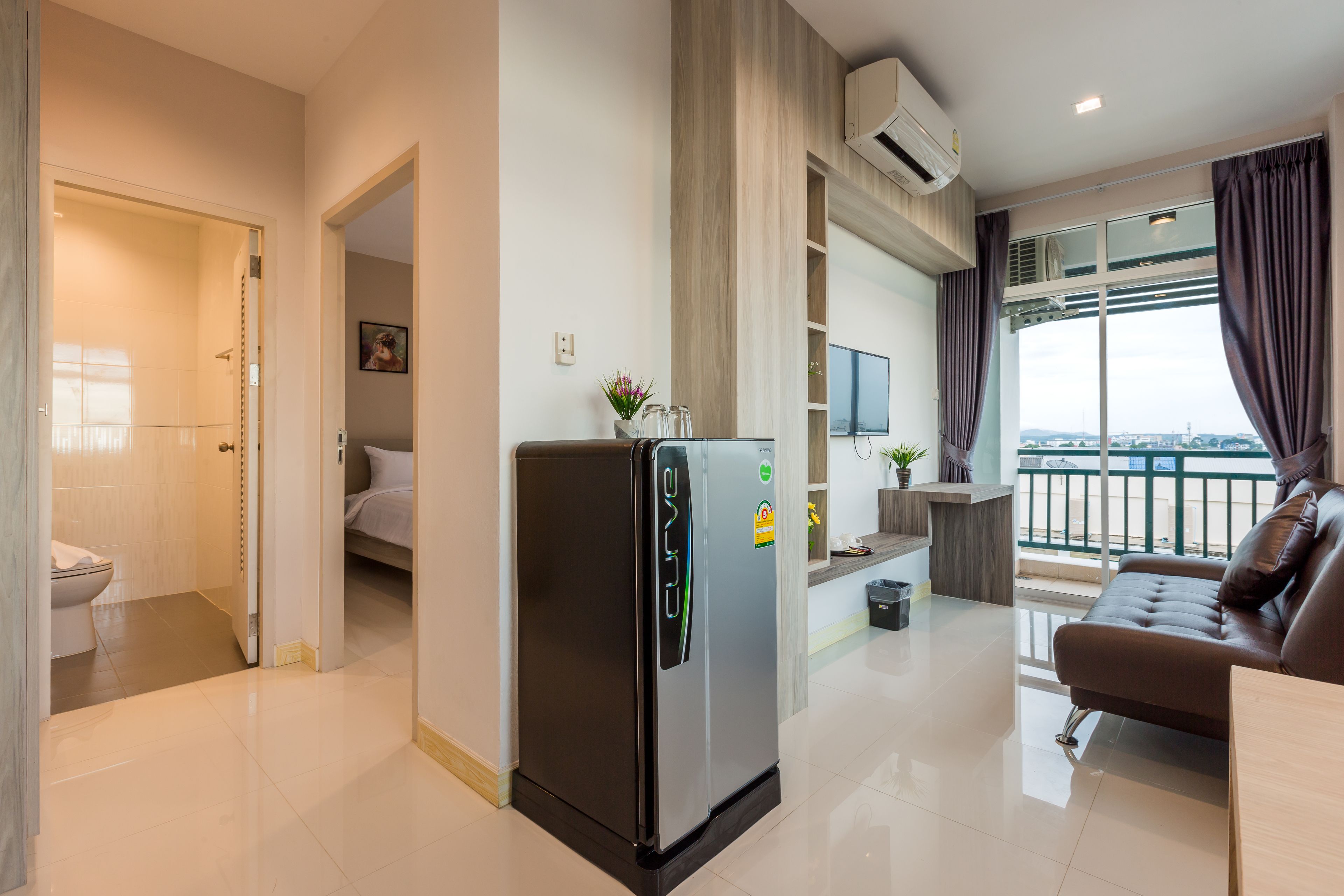 Una habitación de hotel moderna con kitchenette, un balcón con vistas y una sala de estar con sofá y televisor.