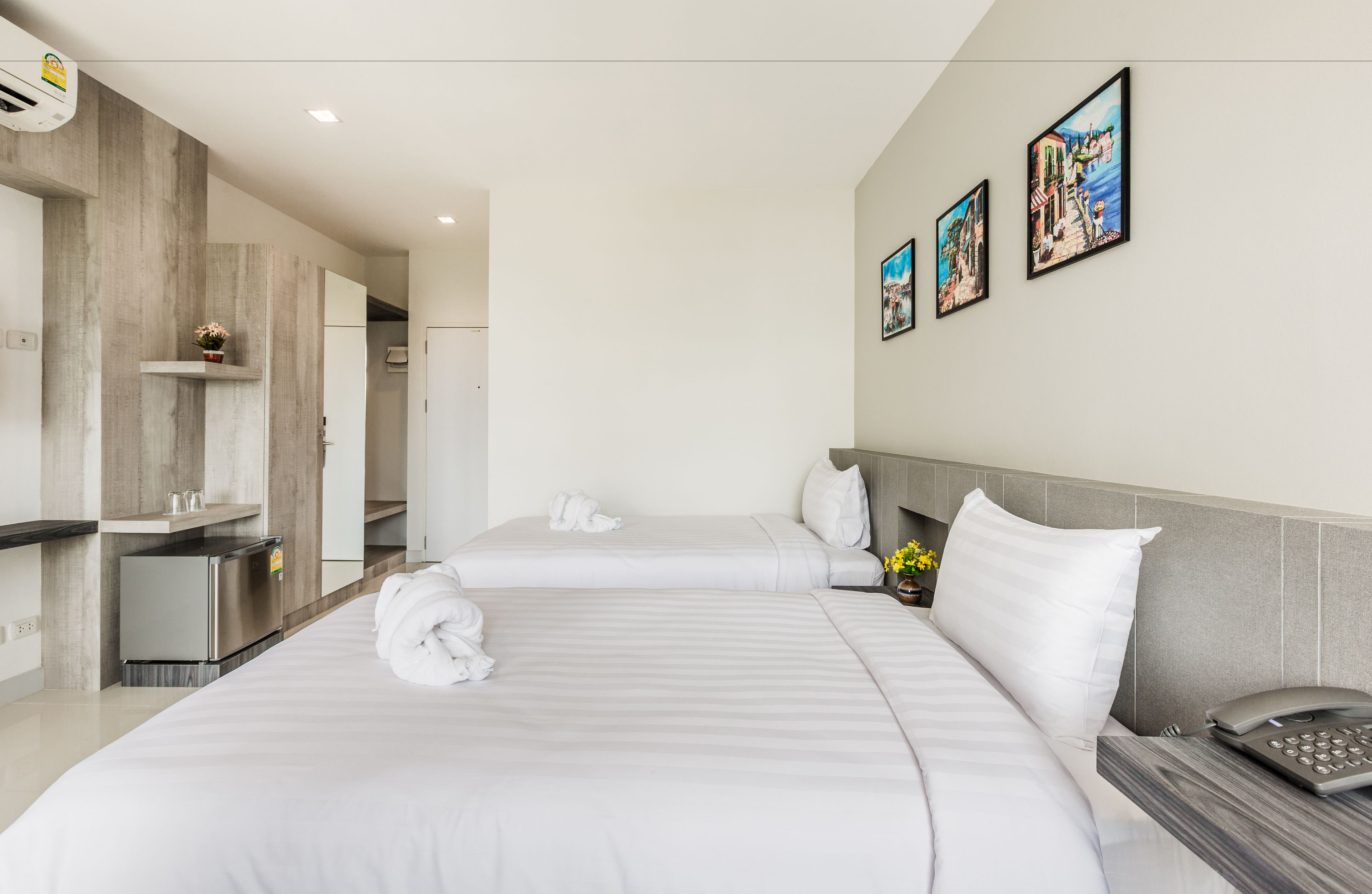 Una habitación de hotel moderna con dos camas, un minibar, un teléfono y obras de arte en la pared.