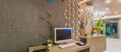 A reception desk with a modern design, featuring a wooden finish and geometric patterns. A computer monitor, keyboard, and phone are placed on the desk.