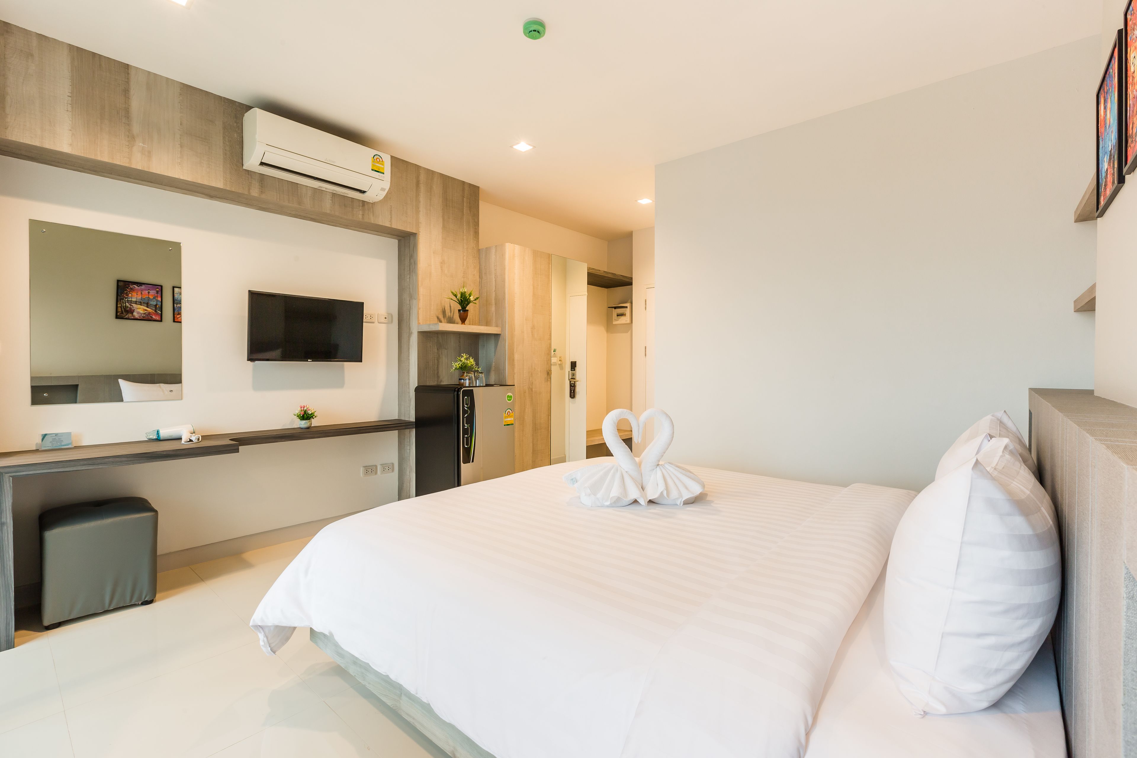 A modern hotel room with a large bed, a desk, a flat-screen TV, and an air conditioning unit.