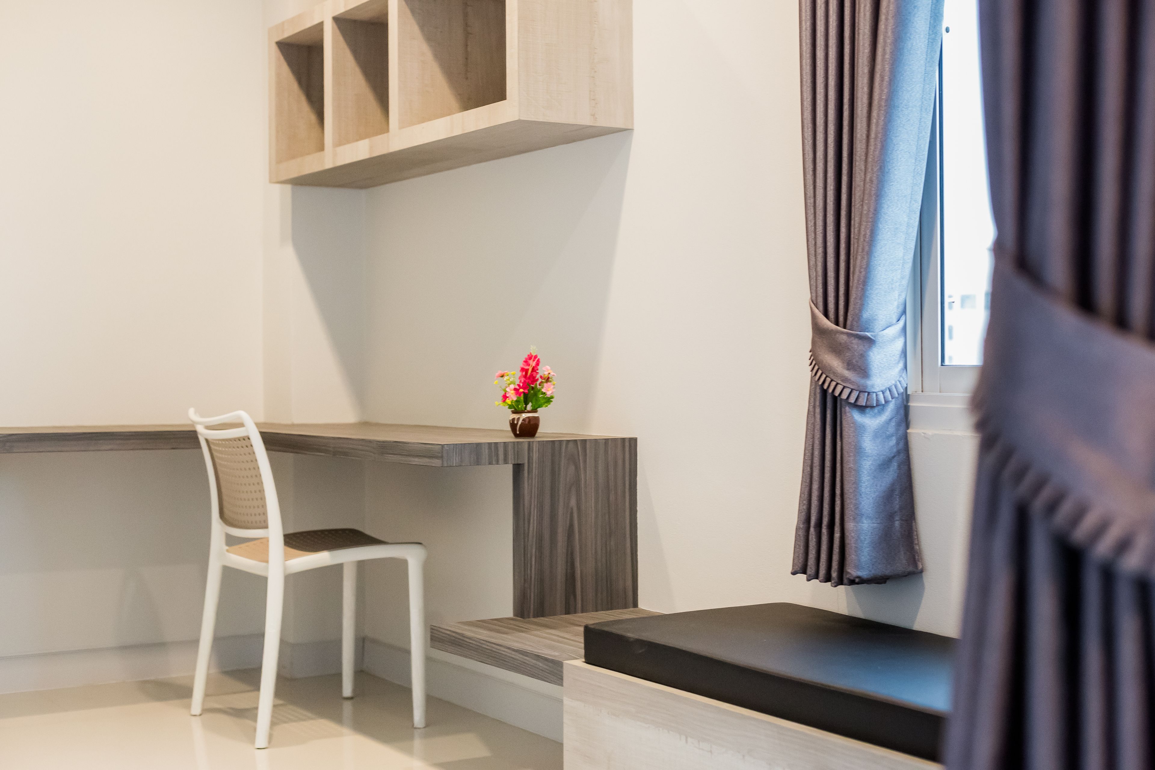A modern room with a desk, chair, and a small table with a flower vase.