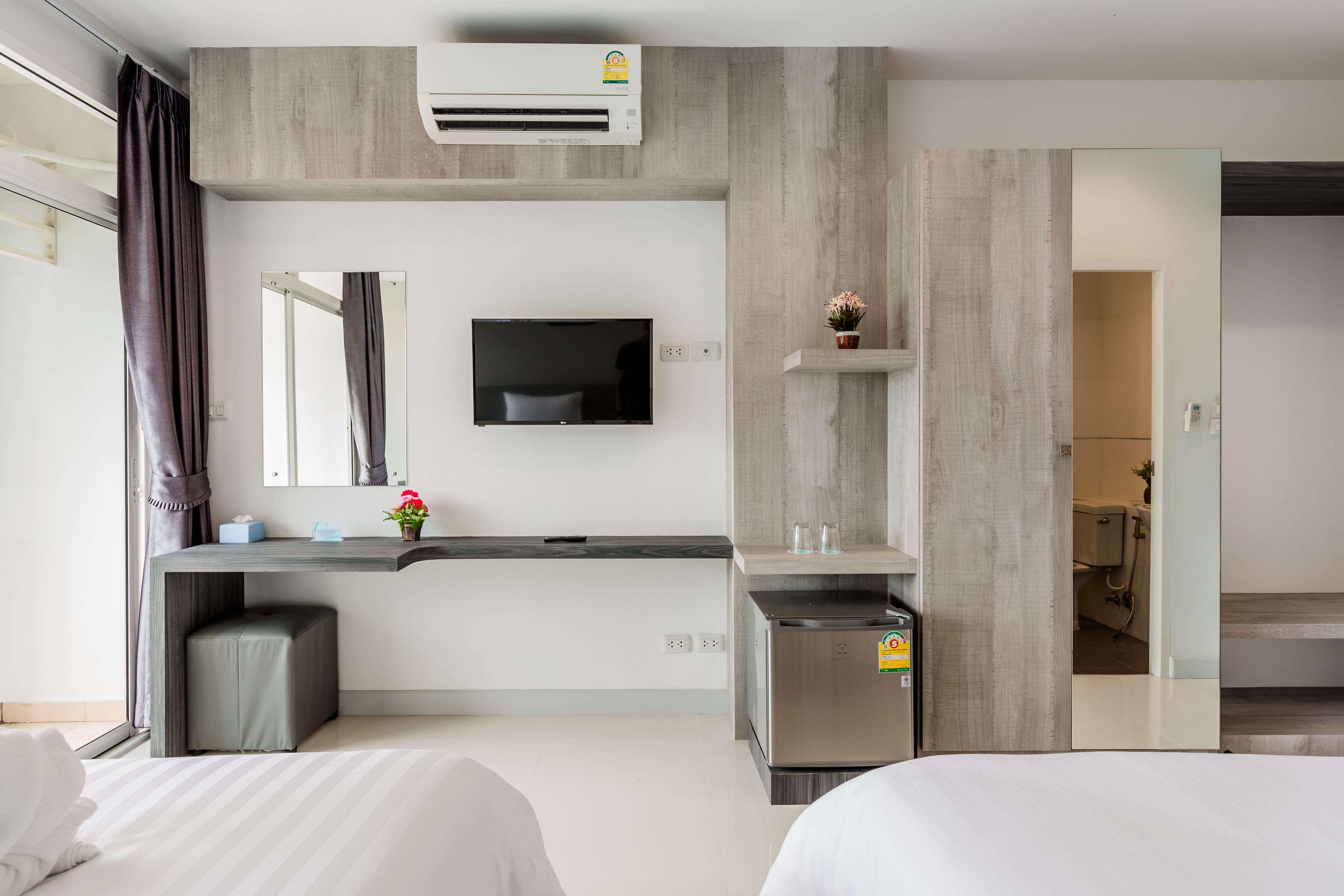 Una habitación de hotel moderna con cama, escritorio, televisor y una kitchenette pequeña.