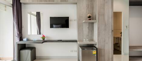 Una habitación de hotel moderna con cama, escritorio, televisor y una kitchenette pequeña.