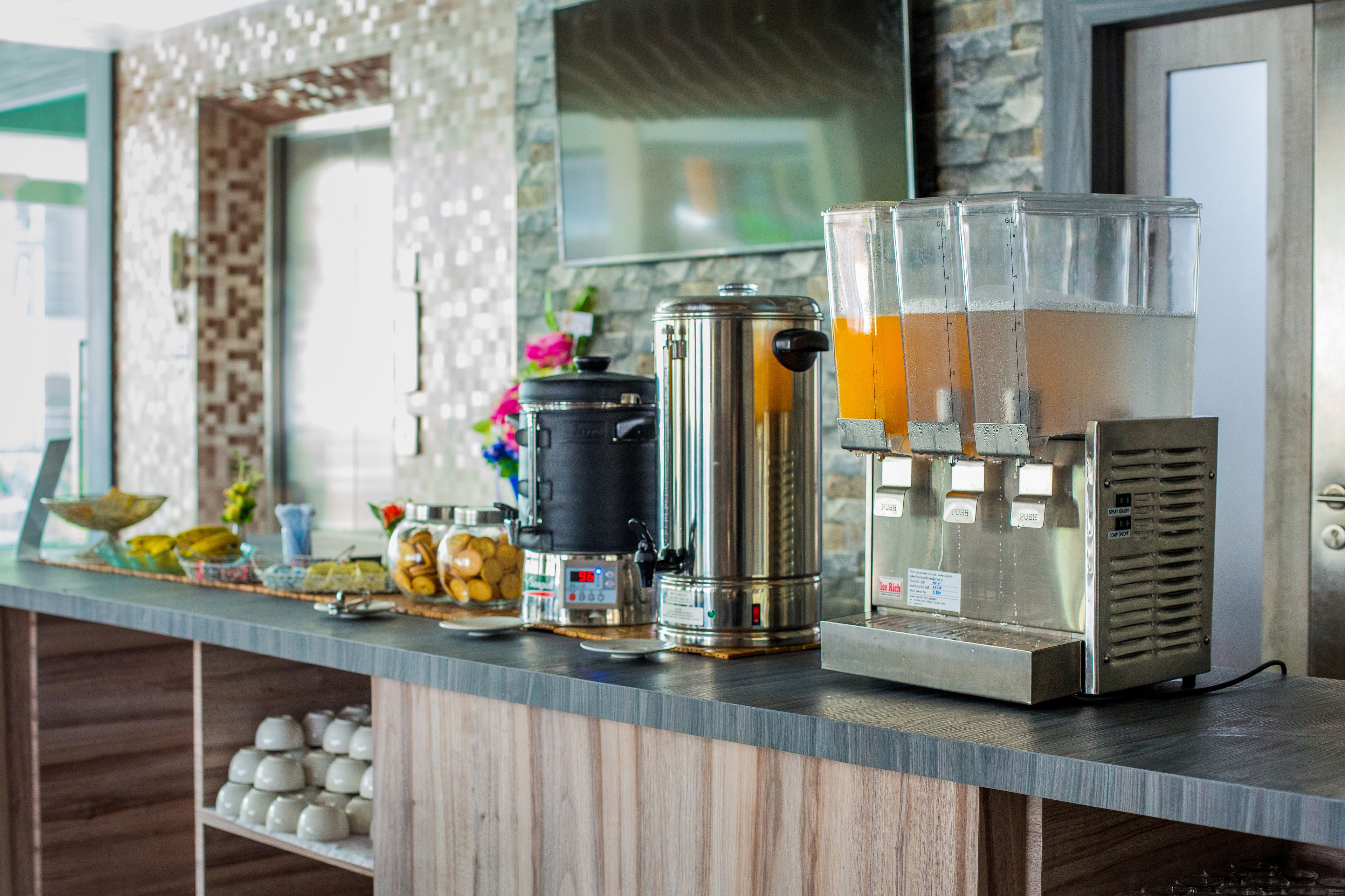 Uma bancada de cozinha com cafeteira, termo e dispensador de suco.