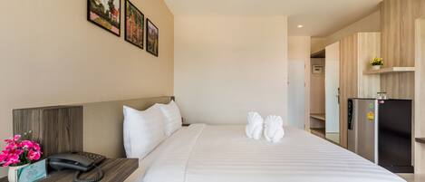 A hotel room with a bed, a desk with a phone, a refrigerator, and a wall with framed pictures.