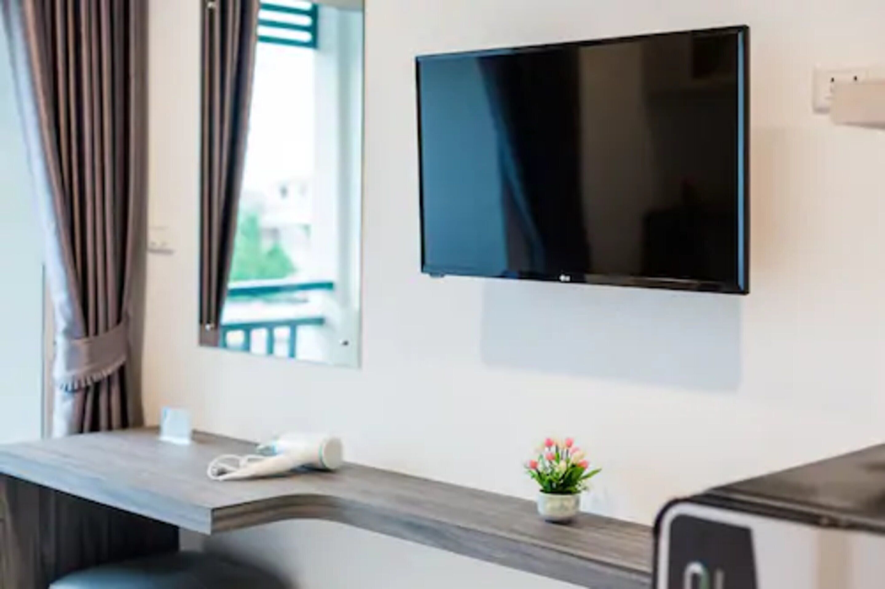 A hotel room with a flat-screen TV mounted on the wall, a wooden desk with a telephone, and a small potted plant.