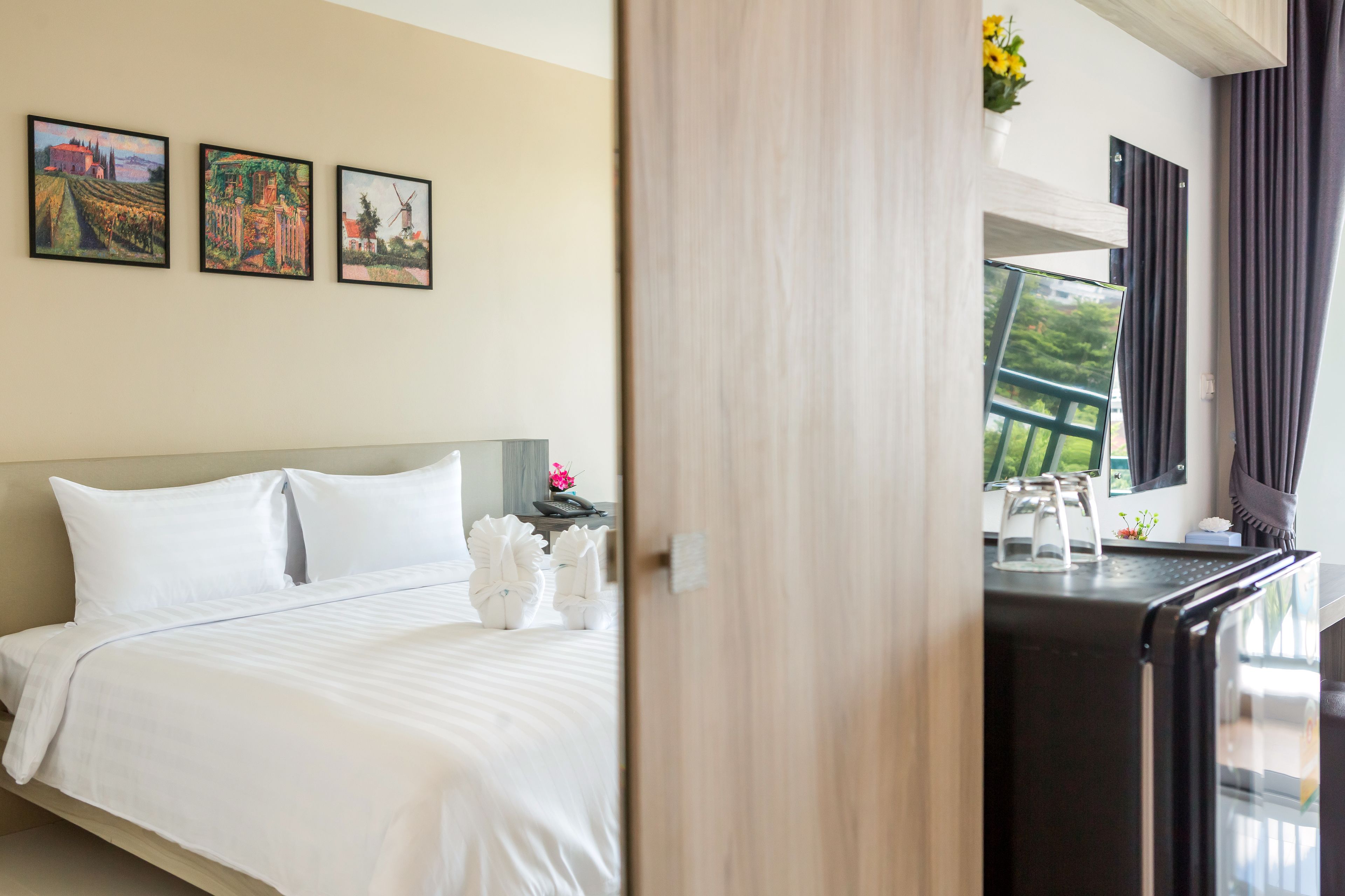 A hotel room with a bed, a nightstand, and a view of the outdoors through a window.